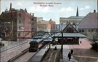 A postcard of a stone Romanesque railway station with a wide canopy in an urban area