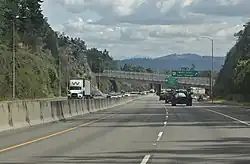 A freeway with four lanes divided by a concrete barrier, looking towards a bridge in the distance.