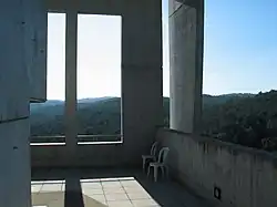 Two chairs on a concrete porch of a rectilinear building overlooking hills and green forest
