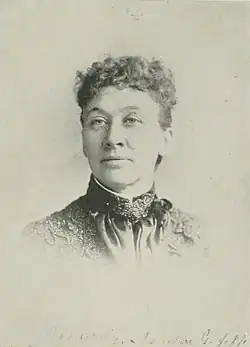 B&W portrait photo of a middle-aged woman with her hair in an up-do, wearing a dark high-collared blouse.