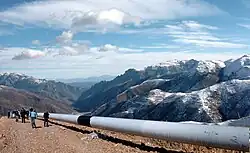 Photo of a large gray pipe with rocky mountains in the background.