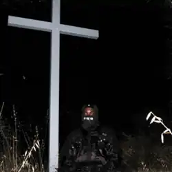 A night scene outside in which a large white cross looms above JPEGMafia, who is covered head-to-toe in black. A small computer mouse is visible floating beside the cross.