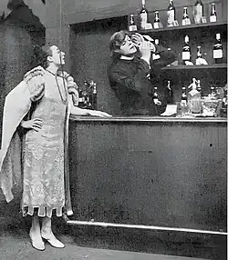 Scene at a bar, with a woman customer and Buchanan in drag, disguised as a barmaid