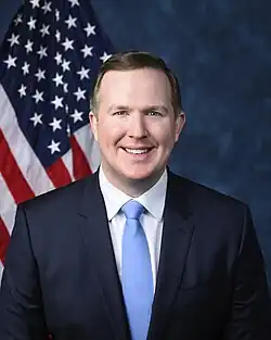 Official House portrait of Jack smiling in front of the U.S. flag, wearing a black suit, white shirt, and blue tie.