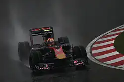 A navy-and-gold single-seater racing car is driven around a drenched tarmac course.