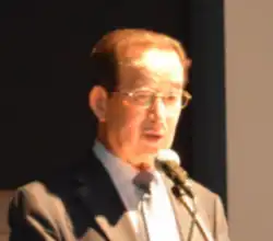 Headshot of Jeong, who wears glasses, speaking in a grey suit