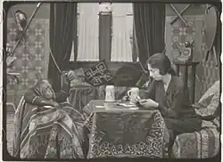 Young orangutan and tall woman with hair pulled back sit at a table; holes from film strip partially visible at left