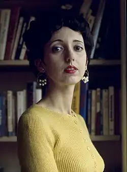 Color portrait of a younger woman standing in front of a bookcase