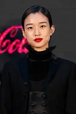 Kawai at press event wearing zebra-print jacket and looking toward camera while smiling