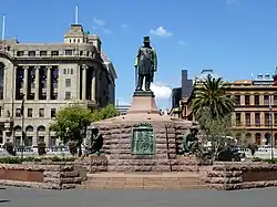 An impressive monument. A statue of Kruger stands on a tall plinth; he is wearing his top hat. Each of the plinth's four sides has a statue of a crouching Boer next to it.