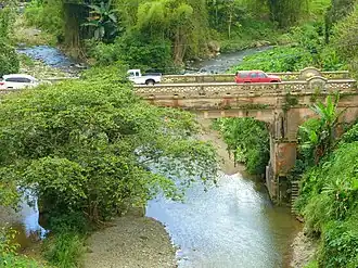 Photograph of a narrow, concrete bridge with traffic, over a small river