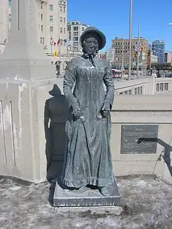 Photo of a statue of a woman in a long dress and a bonnet.
