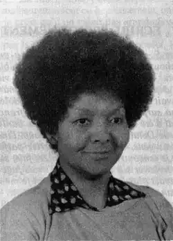 A woman with an afro and a collared shirt smiling