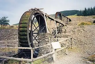 Photograph of two water wheels, one in the foreground and one in the background, each fed water by a wooden launder