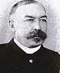 A black and white photo of Louis Carpenter, a white male. He has a mustache and Goutea, his hair is colmbed back and he is wearing a jacket and white shirt