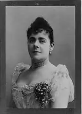Black and white photo of a woman in a formal late 1800s dress.