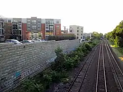 A below-grade railroad corridor, with a retaining wall and housing development at left