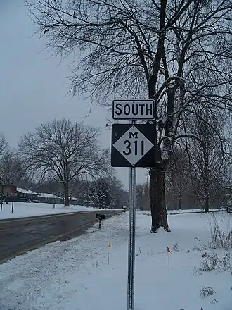 A highway sign alongside the road on a snowy day.