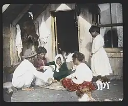 Māori woman and children playing cards on doorstep of their home in Whakarewarewa, 1895
