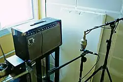 A microphone with a round, silver, head pointed at a guitar amp