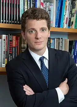Nisbet standing in a business suit with arms crossed in front of bookshelves