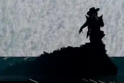 Melody backlit wearing a black dress with a large train.