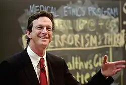 Photograph of Michael Chrichton speaking in front of a chalkboard