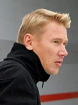 Head and shoulders of a man in his late thirties with blonde hair and grey eyes, facing to the right. He is wearing a black polo neck sweater.