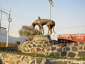 Picture of a monument featuring a dog-shaped sculpture. The dog is depicted a depressed stray dog, with his tail between his legs and one injured hind leg.