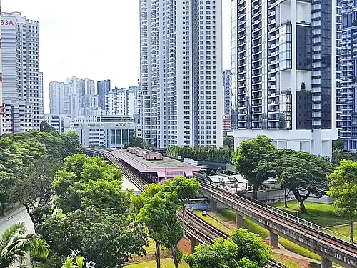 A photograph of Redhill station, the low-lying structure in the middle of the photo, surrounded by trees and high-rise buildings