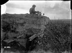 a man sitting atop a partially destroyed concrete bunker with a box in his hand.
