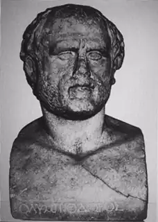 Color photograph of the front of a bronze bust of a man, with the Greek letters for Olympiodors at the base.
