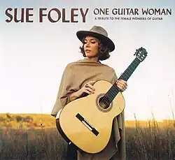 Sue Foley, standing outside and holding an acoustic guitar