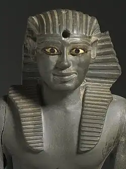 Grey statue of kneeling pharaoh, with vases in its hands