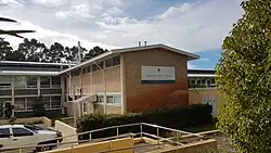 Andrews building is two-storeys high, and consists of a long grey stucco building and a shorter brown brick building which comes off of it at a right angle.