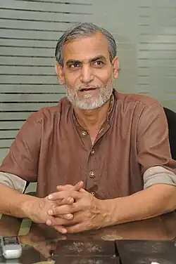 Pervez Bilgrami wearing a brown shirt with rolled-up sleeves, looking left of camera