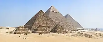 Photo of the Pyramids of Giza, with the three main pyramids at the center against a blue sky in the background