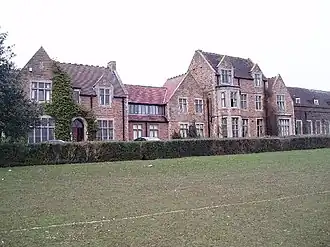 Range of dressed stone Tudor styled buildings stretching left to right, with grass playing fields to front