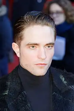 Pattinson with a stern look on his face looking towards a camera