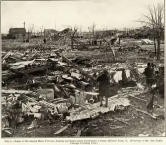 Black-and-white photograph depicting wreckage of building with twisted trees in the background