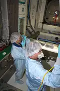 Workers in protective clothing inspect and clean the interior of Node 3