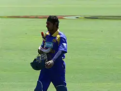 A man wearing blue srilankan jersey holding a bat and a helmet