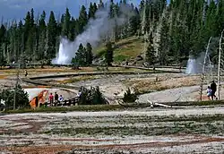 Water and steam shooting from ground as bystanders watch.