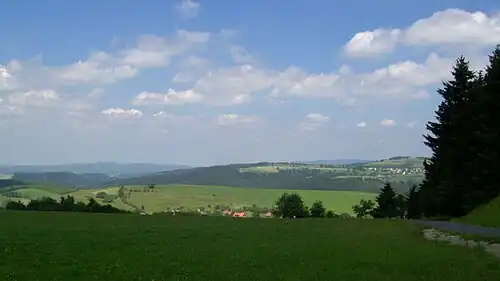 View from the Eckartsberg of Schnett and the Simmersberg (781&nbsp;m, right) with its subpeak, the Kohlberg (718&nbsp;m, centre). Between them in the background can be seen the Adlersberg (849,9&nbsp;m) with the Neuhäuser Hügel (891&nbsp;m). Left of the Kohlberg in the background is the trading estate of Suhl-Friedberg and the Little Thuringian Forest with the Schleusinger Berg (671&nbsp;m) and Schneeberg (692&nbsp;m). Front centre is the village of Waffenrod/Hinterrod.