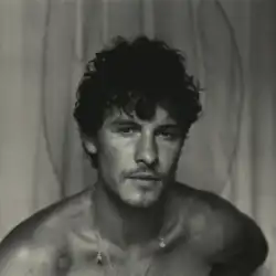 Black and white picture of Shawn Mendes facing the camera in front of a curtain.