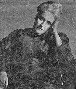 Portrait of an older woman with white hair. She is seated with her head leaning into her hand.