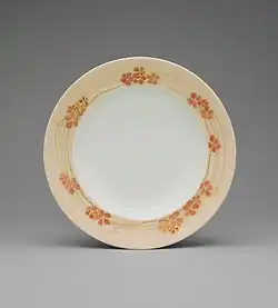 A white shallow bowl with a border of light orange with darker orange flowers and gold streaks.