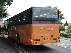 Rear of orange and brown 'fountain'-branded Premiere coach with horizontal taillights and a curved rear window