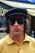 Jackie Stewart wearing a yellow T-shirt, a black cap and sunglasses