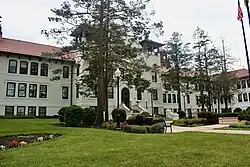 A tall white building, with two towers one either side of the main entrance, which has stairs. A paved path cuts through grass to the entrance.